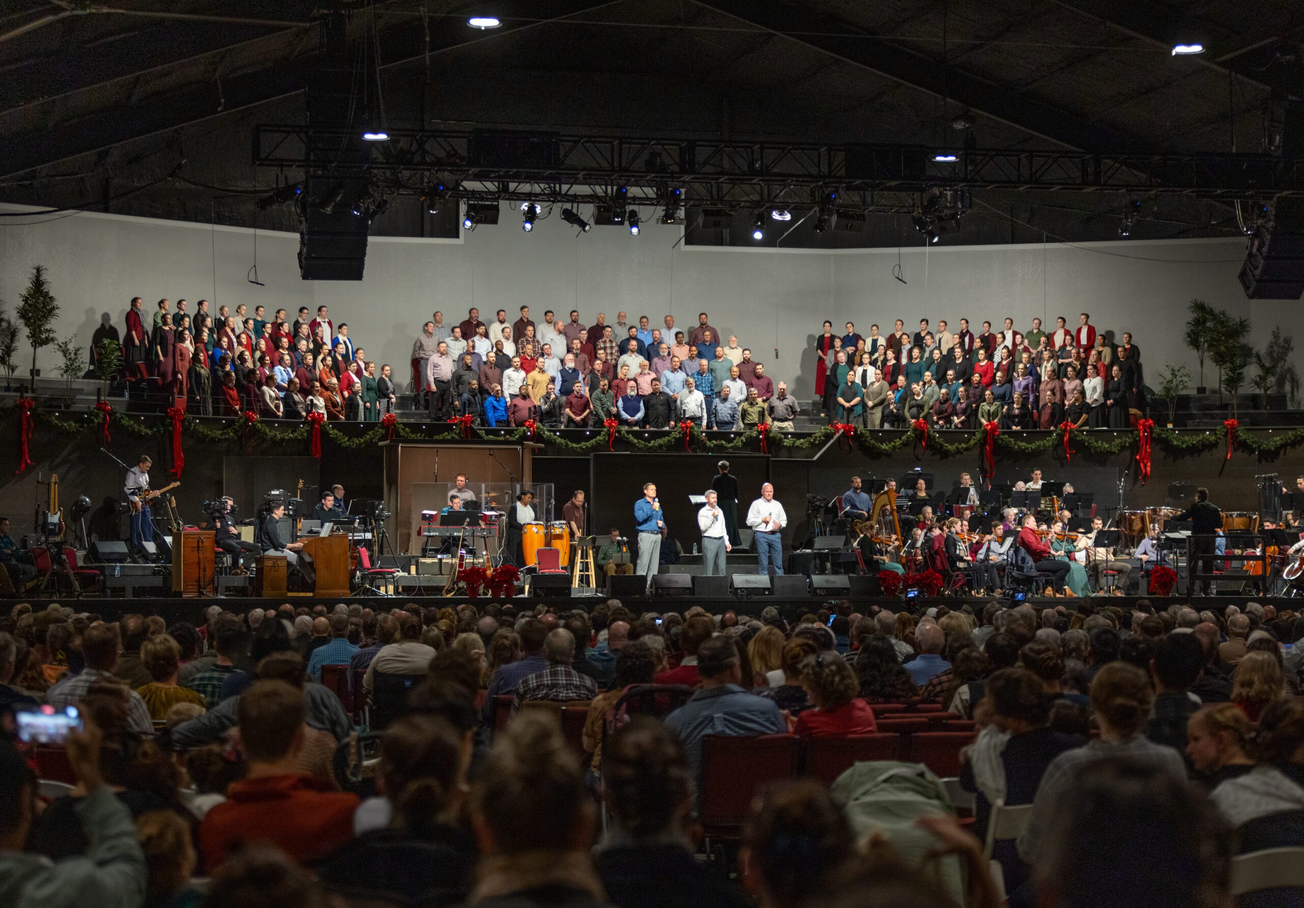 Choir and orchestra performing on a stage hung with garland and red bows at Homestead